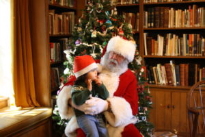 The 2019 Cocoa with Santa events will be held three days December 5, 6, and 7. Tickets on sale November 1, 2019. (Photo - Santa w a child on lap in front of Christmas Tree)