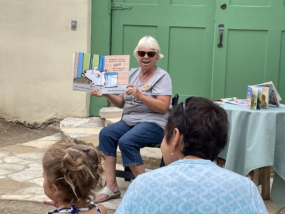 Rancho Los Cerritos Storytime Reader presenting book to a mother and child