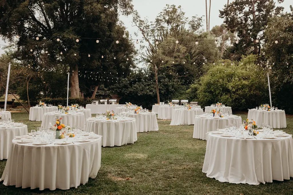 Outdoor wedding reception setup with round tables and lights.