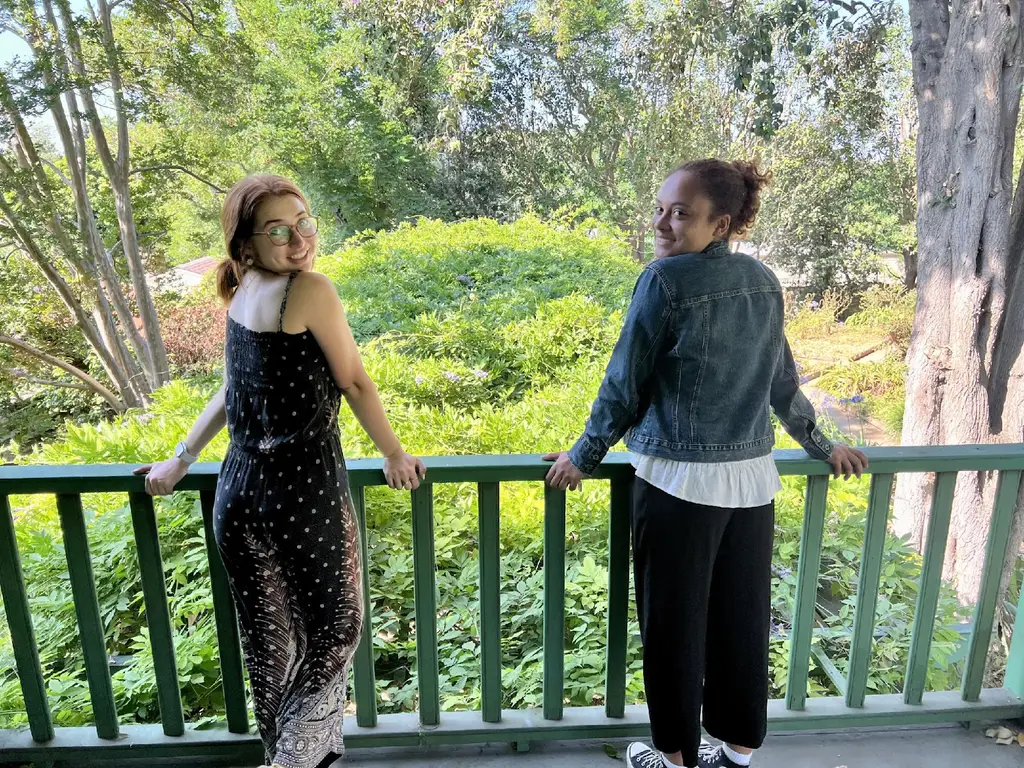 Two women smiling on balcony overlooking greenery.