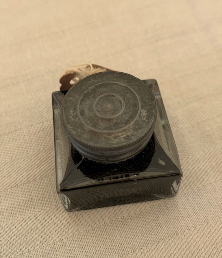 Old ink bottle on beige fabric surface.