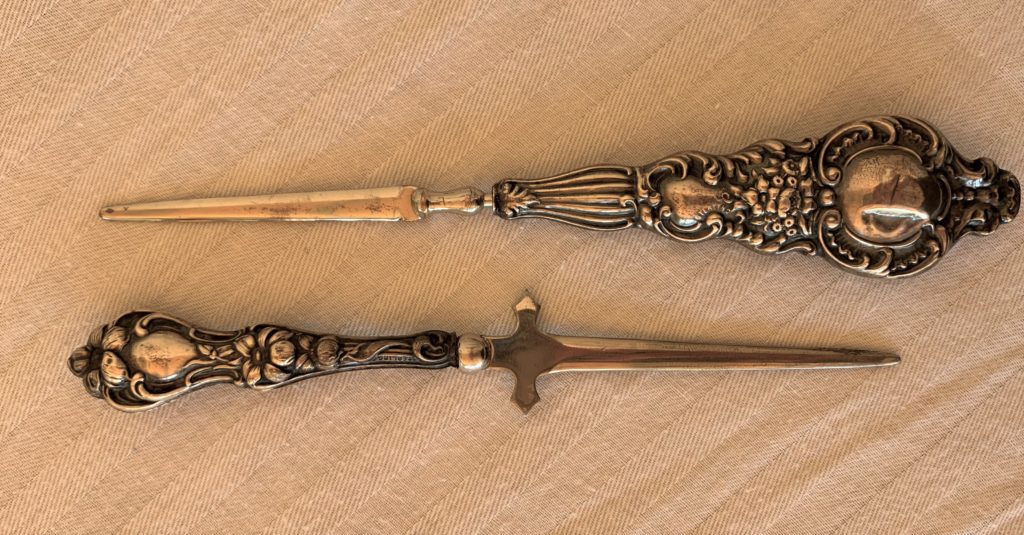Two ornate silver letter openers on fabric surface.