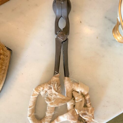 Antique iron tool with wrapped handles on marble table.