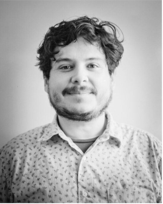 Smiling person with curly hair wearing patterned shirt.