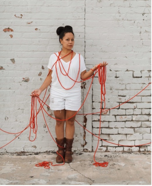 Person tangled in red ropes against brick wall.