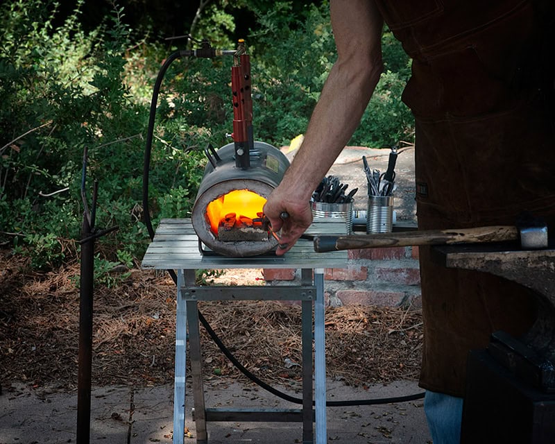 Blacksmith working at outdoor forge with tools.