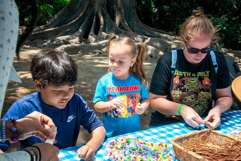 Kids crafting with beads at picnic table.