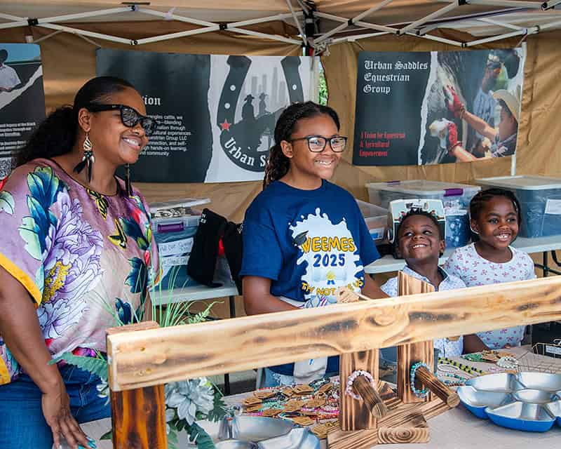 Family smiling at outdoor event booth.