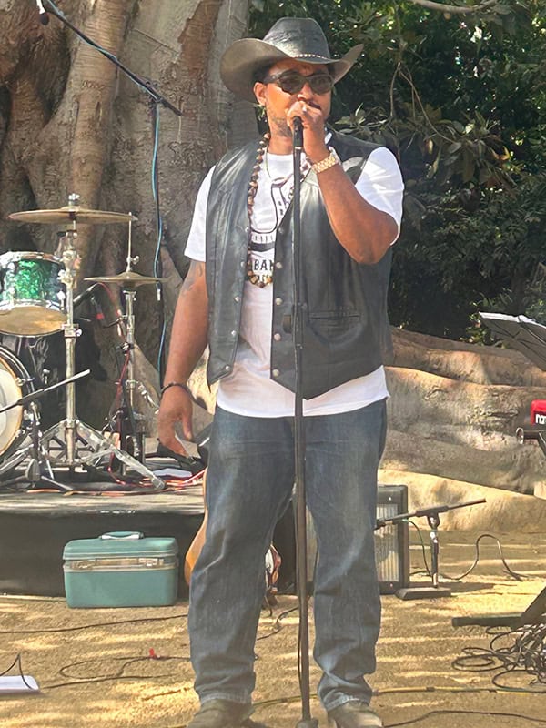Singer performing outdoors with drums in background.
